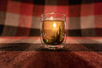 A transparent cup of herbal tea by the light of a burning candle. Close-up