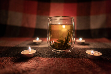 A transparent cup of herbal tea stands in a circle of burning candles
