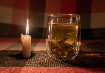 A transparent cup of herbal tea by the light of a burning candle. Close-up