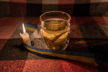 A transparent cup of herbal tea by the light of a burning candle with a yellow-blue ribbon
