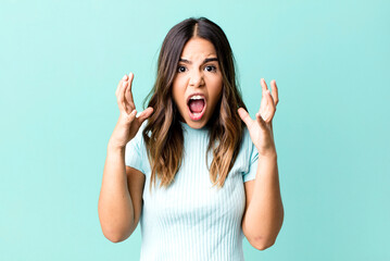 hispanic pretty woman screaming with hands up in the air, feeling furious, frustrated, stressed and...