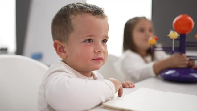 Adorable girl and boy sitting on table learning of planets at kindergarten