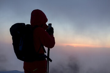 Tourist with mobile camera on the background of sunrise in the foggy winter mountains