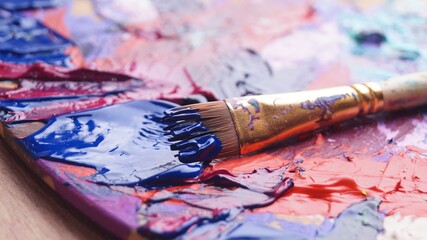 Brush and artist's palette with mixed paints on wooden table, closeup