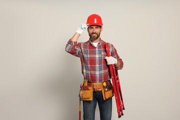 Professional builder in hard hat with tool belt and step ladder on light background