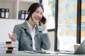 Pretty Asian business woman in black suit working at her office desk, with document file and paperwork. make a call mobile smartphone