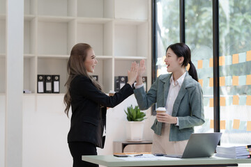 Female business worker with colleagues in Thailand working together at office desk, getting high five, teamwork concept