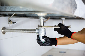Technician plumber using a wrench to repair a water pipe under the sink. Concept of maintenance,...
