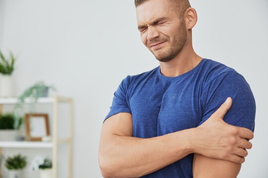 A man has pain in his arm, sprain of muscles and ligaments during sports, inflammation and injury, in a blue t-shirt at home