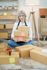 Starting small business entrepreneur of independent Asian woman smiling using computer laptop with cheerful success of online marketing package box items and SME delivery concept