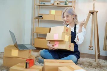 Starting small business entrepreneur of independent Asian woman smiling using computer laptop with cheerful success of online marketing package box items and SME delivery concept