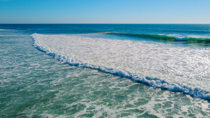 Sea waves with white foams rolling in on the beach in Huntington Beach, California