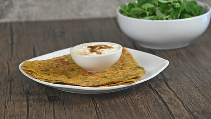Methi paratha Indian flat bread made with wheat flour , fenugreek leaves  and spices.  Methi paratha served in a plate with Yogurt.