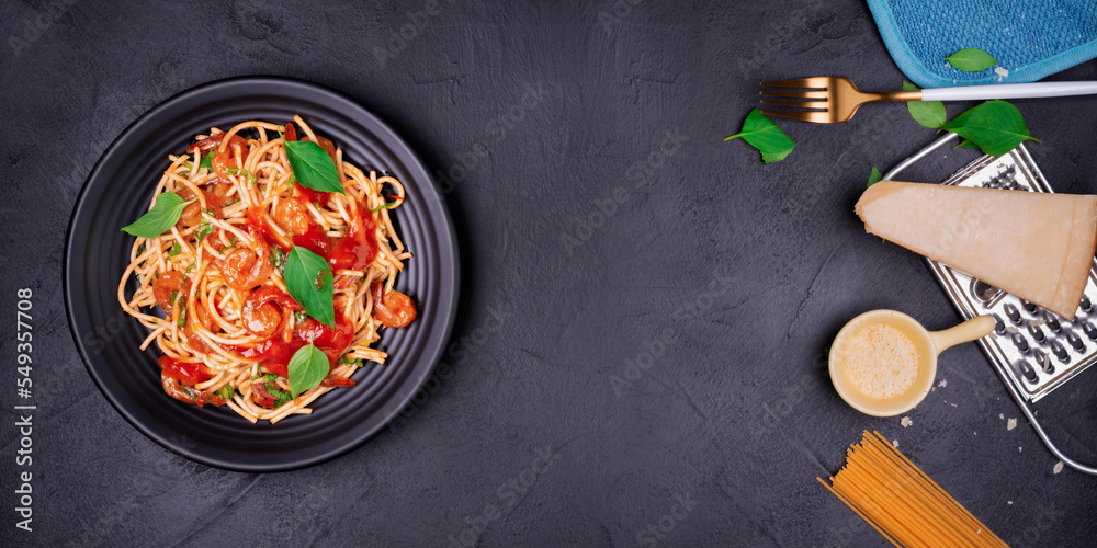 Wall mural Delicious spaghetti pasta with prawns and cheese served on a black plate on a black background table Italian recipe, tomato sauce, vegetables, and spices top view with copy space