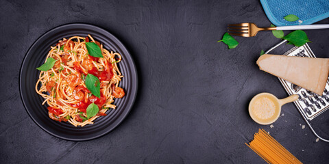 Delicious spaghetti pasta with prawns and cheese served on a black plate on a black background table Italian recipe, tomato sauce, vegetables, and spices top view with copy space