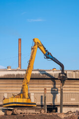 Yellow Pile drilling crawler crane working to install foundation near the old factory building in industrial construction site