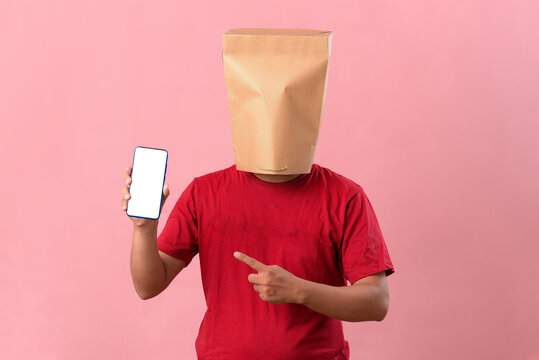 Concept portrait of Asian man with head covered with paper bag pointing at phone screen