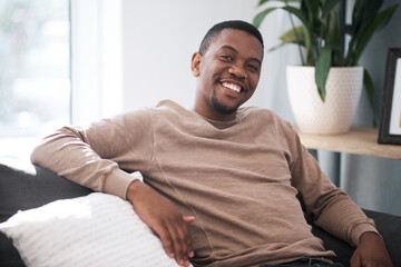 Relax, smile and portrait of black man on sofa at home in city apartment. Happy, healthy and proud man and leader in business from South Africa smiling and relaxing alone on couch in living room.