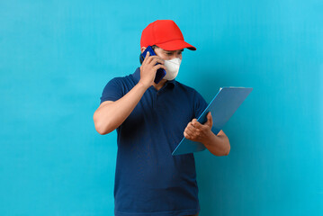 Asian Delivery man talking on a mobile phone and holding a clipboard of checklist, wearing face mask