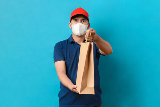Delivery service man wearing face mask with blue uniform holding a packet paper bag