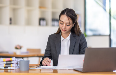 Fototapeta na wymiar Asian female business analyst financial advisor preparing statistic report studying documents on work desk, Asian business woman work with documents in the office.