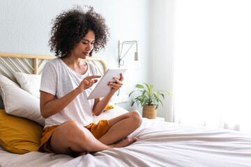 Young multiracial woman using sitting on bed down relaxing at home cozy bedroom. Copy space.