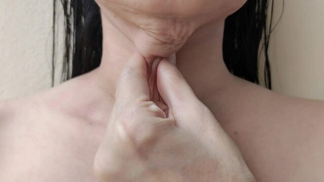 portrait the fingers squeezing the flabbiness adipose hanging skin under the neck, wattle and flabby skin under the chin, problem wrinkles on the body of the woman, health care and beauty concept.