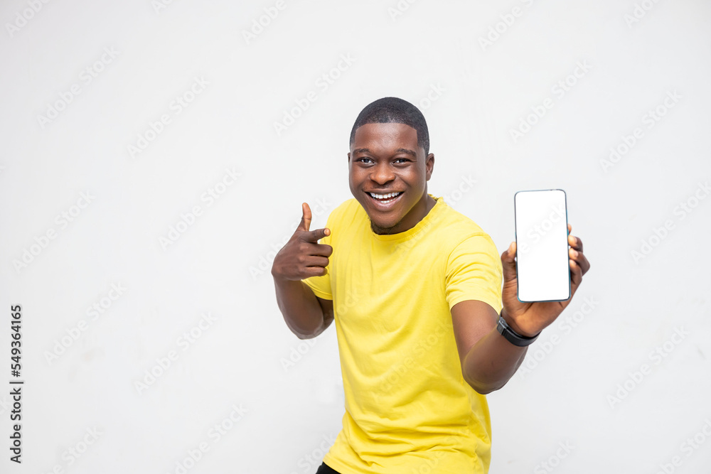 Wall mural handsome young african man holding smartphone mockup of blank screen and pointing at the phone over 