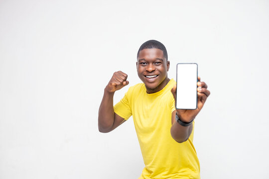 Over Excited Young African American Man Holding Smartphone Mockup Of Blank Screen Celebrating Over A White Background