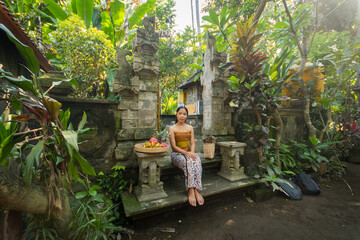 Young Asia woman near a temple and carries a tropical fruit, pineapple, dragon fruit and bananas.