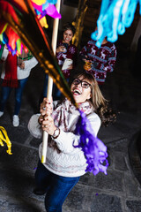 Hispanic mature woman with Mexican family breaking a piñata at traditional posada party for...