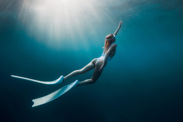 Freediver woman with white fins underwater. Freediving with beautiful girl in ocean and sun rays