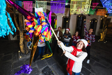 Fototapeta na wymiar Hispanic young girl with Mexican family breaking a piñata at traditional posada party for Christmas in Mexico Latin America