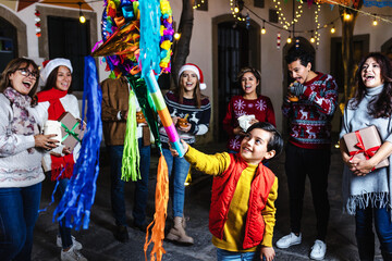 Hispanic child boy with Mexican family breaking a pinata at traditional posada party for Christmas...