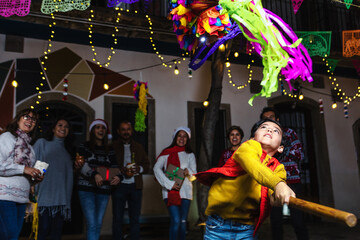 Hispanic child boy with Mexican family breaking a pinata at traditional posada party for Christmas...