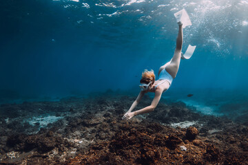 Woman freediver in white swim wear dive with fins over corals. Freediving in tropical blue ocean