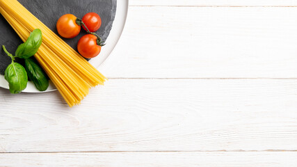 Cherry tomatoes, basil, raw pasta for spaghetti on white wooden table