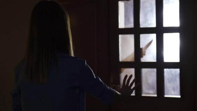 The woman is afraid of the psychopathic man who has a shadow in the dark at home.
Female abuse. Man silhouette holding knife scares woman in concept of violence and harassment against women.
