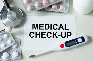 On the white card inscription MEDICAL CHECK-UP next to pills, stethoscope, thermometer. Medical and health care concept.