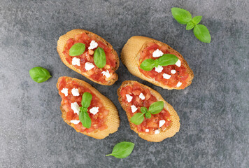 Delicious slices of Italian tomato bruschetta with fresh basil on a gray background, top view. Italian appetizers.