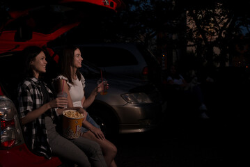 Two female friends with popcorn sitting in the car while watching a movie at drive in cinema....