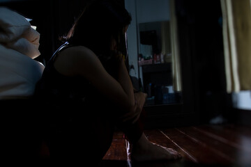 Asian girl suffering from depression sitting on the floor near her bed side, sad women sitting in...