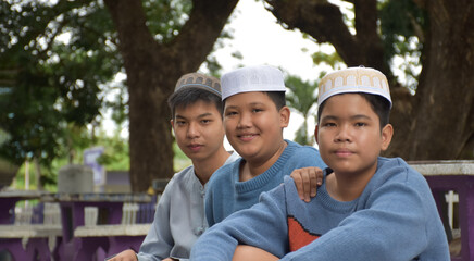 Young asian muslim or islamic boys sitting together in the school park to read, to learn, to do and to consult homework and waiting to learn religious subjects at school, soft and selective focus.