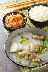 Soegogi muguk Beef and radish soup is a very popular soup in Korea served with rice and kimchi closeup on the mat on the table. Vertical