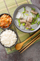 Korean Beef Radish Soup Sogogi Muguk served with rice and kimchi closeup on the mat on the table. Vertical top view from above