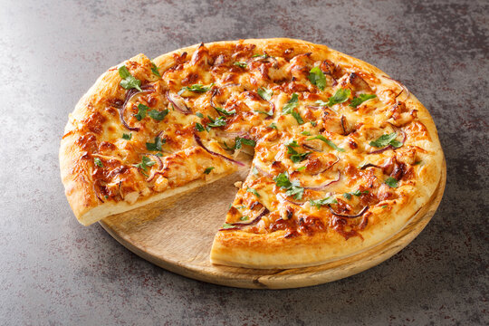 Chicken BBQ pizza made of pieces of chicken with a spicy sauce with toppings of onions, mozzarella cheese and cilantro closeup on the wooden board on the table. Horizontal