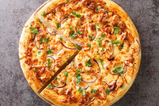 Chicken BBQ pizza made of pieces of chicken with a spicy sauce with toppings of onions, mozzarella cheese and cilantro closeup on the wooden board on the table. Horizontal top view from above