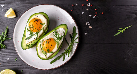 Avocado baked with eggs, fresh arugula, ground pepper on dark background, top view