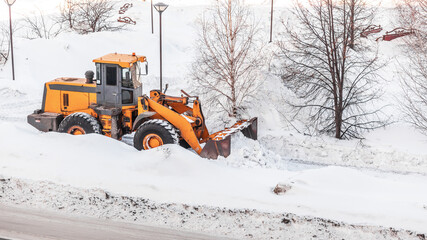 Snow clearing. Tractor clears the way after heavy snowfall. A large orange tractor removes snow from the road and clears the sidewalk. Cleaning roads in the city from snow in winter.