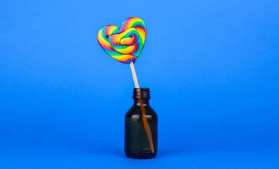 Rainbow colored heart shaped lollipop in small bottle on blue background